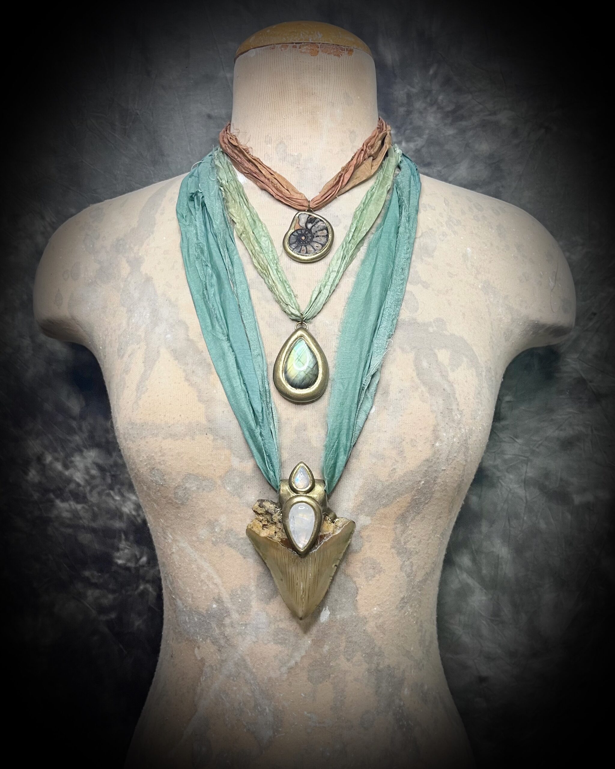 Crystal healing layering necklaces by Become Spellbound featuring a genuine megalodon shark tooth fossil with rainbow moonstones, labradorite crystal necklace and ammonite fossil pendant all hung o recycled silks.